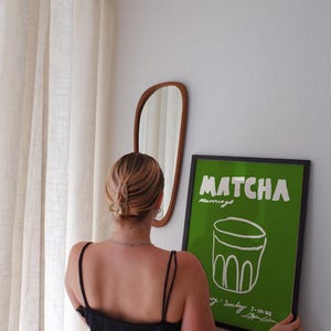 May include: A framed rectangular poster with a vibrant green background featuring the white text MATCHA mornings and a white line drawing of a glass. The poster includes additional white text at the bottom reading Sunday 7-10:00.