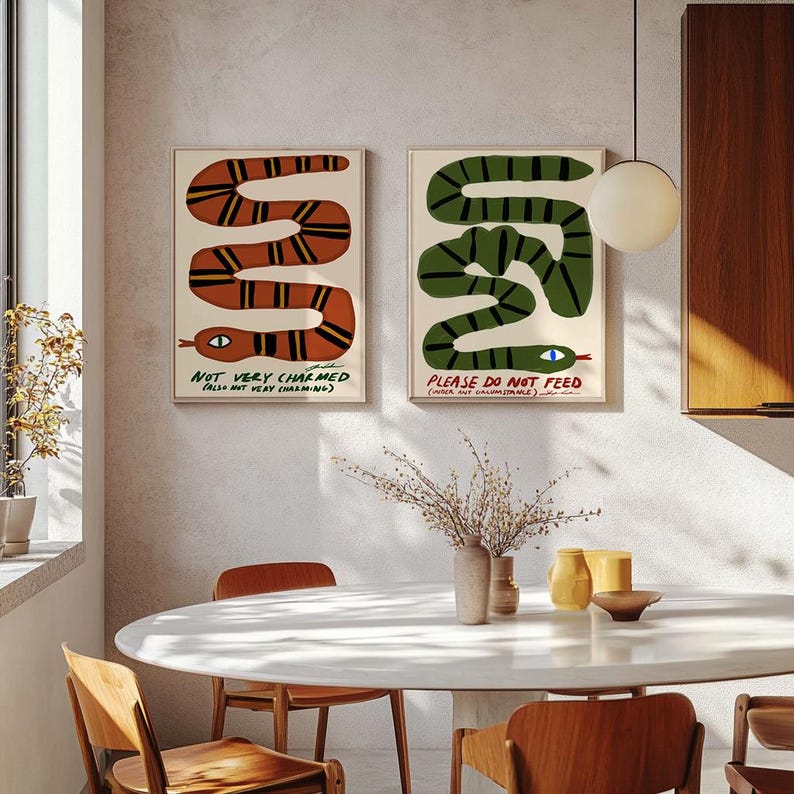 May include: Two framed art prints with snake illustrations. One shows an orange snake with black stripes and the text "NOT VERY CHARMED". The other features a green snake with black stripes and the text "PLEASE DO NOT FEED".