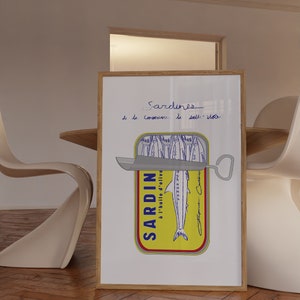 Chic Hand-drawn minimalist kitchen and bar cart print "Sardines" art print poster by KunstbyStephie. A framed print of a hand-drawn illustration of a sardine can with the text 'Sardines - de la Conserverie de la Belle-Iloise' above the can. The can is yellow with a blue label that says 'SARDIN à l'huile d'olive' and a blue drawing of a sardine. The can is open with a silver can opener on top. The print is on a white background and is framed in a light brown wood frame.