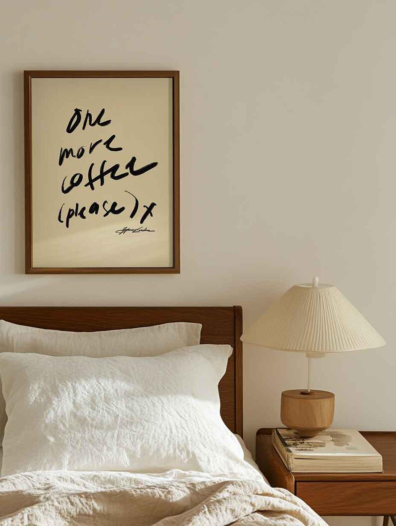 Puede incluir: Un cuadro enmarcado con el texto "One more coffee (please) x" en escritura negra. El cuadro cuelga sobre una cama con ropa de cama blanca, un cabecero de madera y una l&aacute;mpara de noche con una pantalla color crema.