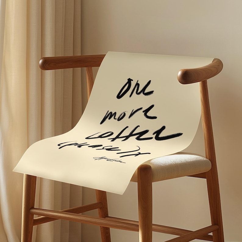 Puede incluir: Silla de madera con asiento y respaldo crema. Una hoja de papel crema est&aacute; sobre el respaldo, con la frase manuscrita "One more coffee please" en tinta negra.