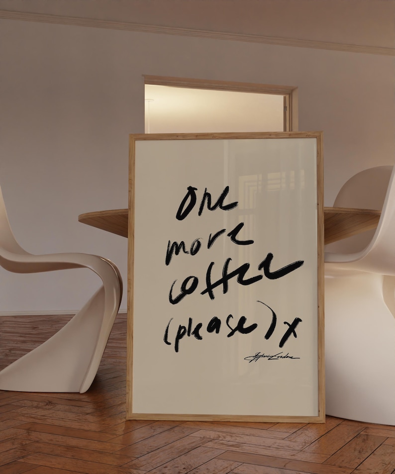 Puede incluir: Una impresi&oacute;n art&iacute;stica enmarcada con las palabras "one more coffee (please) x" en escritura negra. La impresi&oacute;n tiene un fondo beige claro y un marco de madera natural. La obra de arte se exhibe en una habitaci&oacute;n con sillas blancas y una mesa de madera.