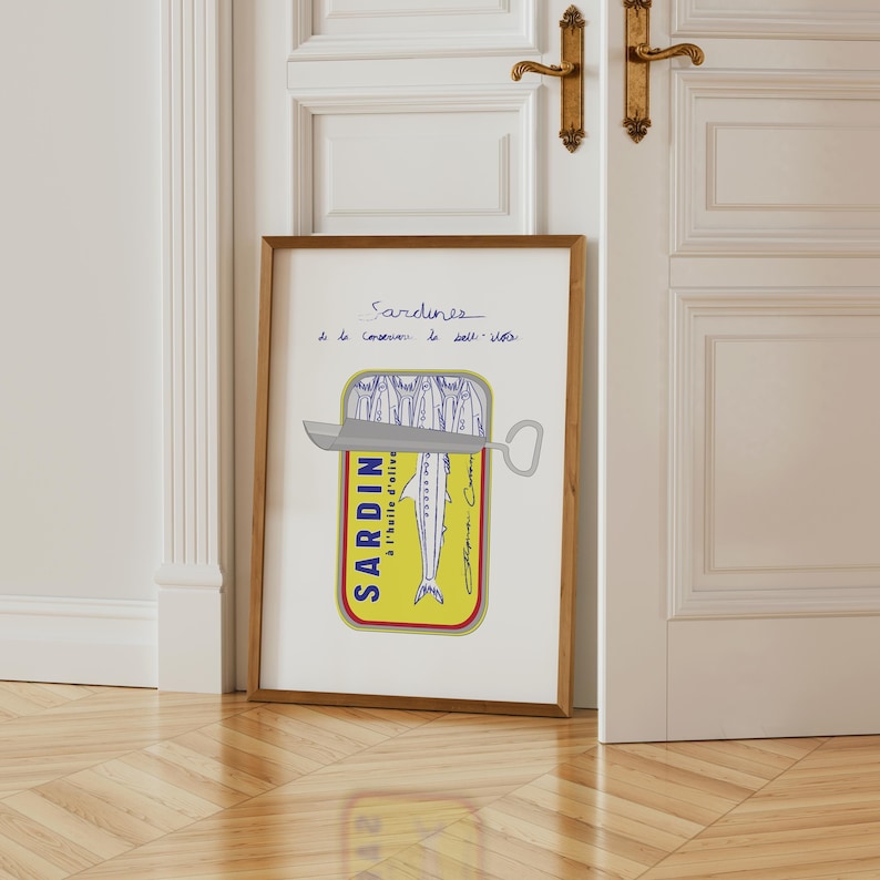 Pu&ograve; includere: Una stampa incorniciata con un'illustrazione stilizzata di una scatoletta di sardine. La scatoletta &egrave; gialla con la parola "SARDIN" in blu e un disegno di un pesce. La stampa include testo scritto a mano in inchiostro blu.