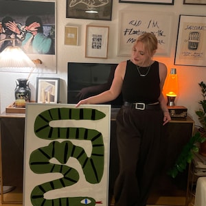 May include: A framed artwork depicting a green snake with black stripes against a white backdrop. The text "PLEASE DO NOT FEED (UNDER ANY CIRCUMSTANCE)" is at the bottom. The print is displayed in a room with other framed artworks.