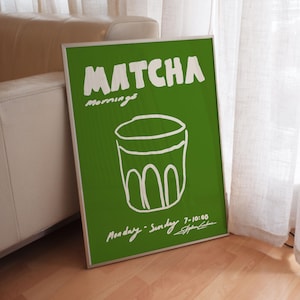 Framed typography poster lime green featuring matcha drink food illustration and bold lettering by KunstbyStephie, styled in a contemporary minimalist living room with beige leather sofa and linen curtains.