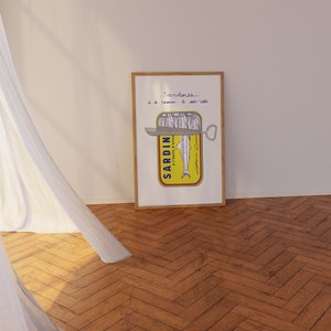 Chic Hand-drawn minimalist kitchen and bar cart print "Sardines" art print poster by KunstbyStephie. A framed print of a yellow sardine can with a silver can opener. The can is labeled 'SARDIN - A L'HUILE D'OLIVE' and has a drawing of a sardine inside. The text above the can reads 'Sardines a la conserve - le sel - sel - sel'.