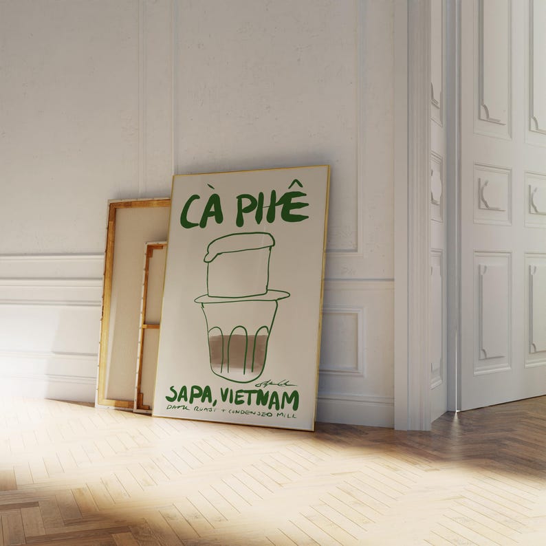 May include: A framed poster with the words "C&agrave; Ph&ecirc;" in green, depicting a Vietnamese coffee filter and cup. The text "Sapa, Vietnam" is below the illustration, with additional text about the coffee. The poster leans against a wall.