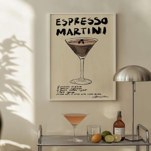 May include: A framed print with the words "ESPRESSO MARTINI" in black lettering. Below the title is a drawing of a cocktail glass filled with a dark liquid. The recipe is handwritten below the drawing. A cocktail glass and ingredients sit on a shelf.
