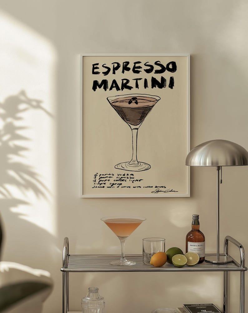 May include: A framed print with the words "ESPRESSO MARTINI" in black lettering. Below the title is a drawing of a cocktail glass filled with a dark liquid. The recipe is handwritten below the drawing. A cocktail glass and ingredients sit on a shelf.