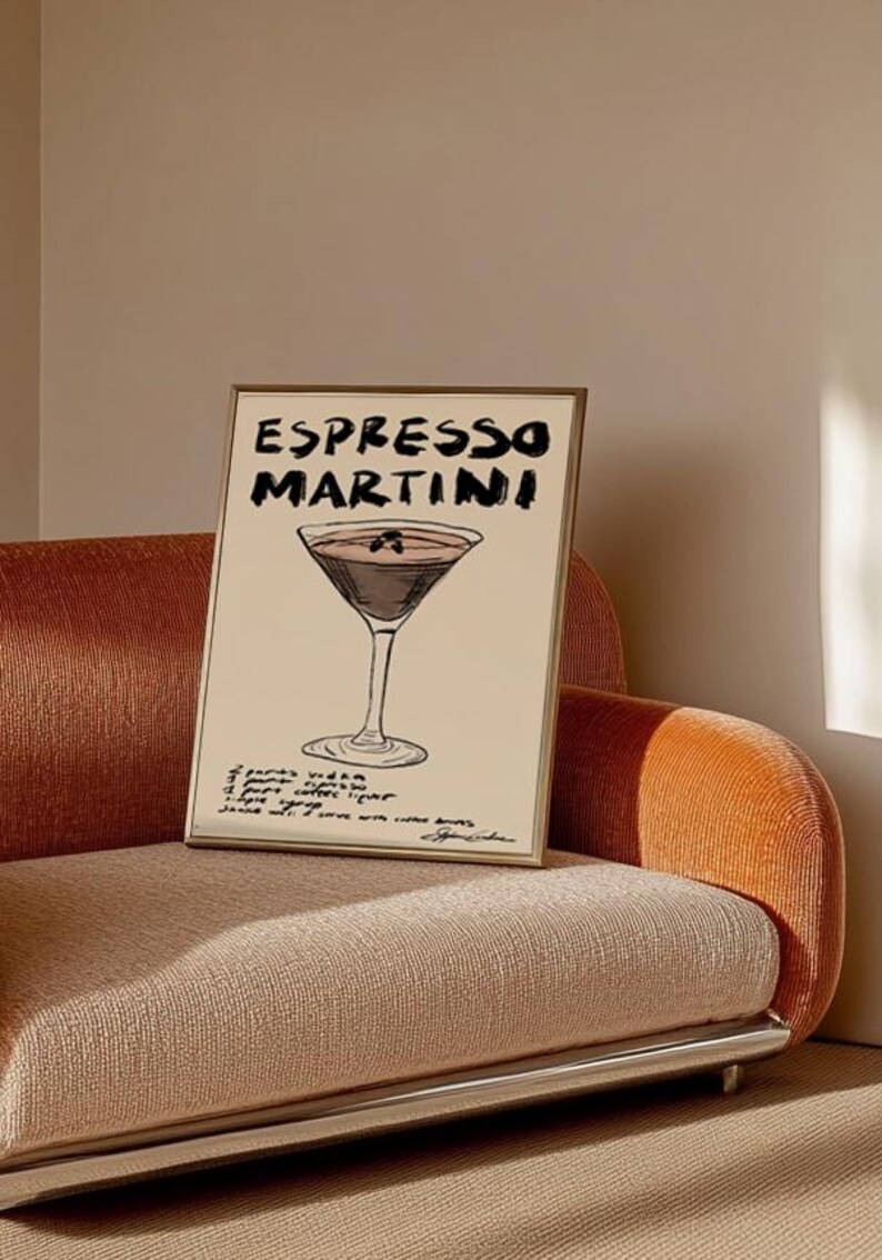May include: A framed print with an Espresso Martini design. The words "ESPRESSO MARTINI" are written in black above a cocktail illustration. The recipe is below the image. The frame is gold. The print is displayed on a peach-colored sofa.