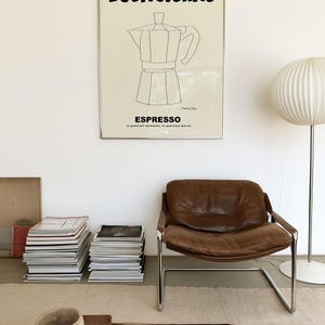 May include: A rectangular wall art print in a thin silver frame featuring a cream background with black text that reads BUONGIORNO and ESPRESSO, along with a black line drawing of a moka pot and the small signature of the artist at the bottom.