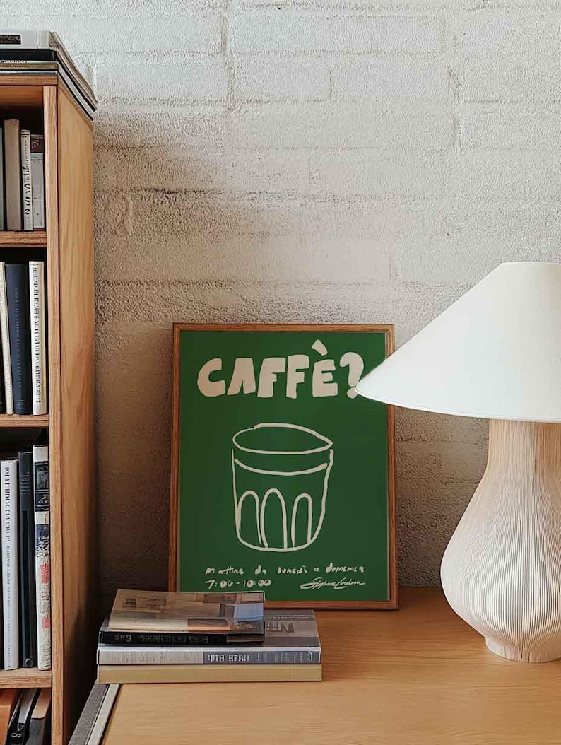 Op de afbeelding: Een groene poster met het woord "CAFF&Egrave;?" in het wit en een tekening van een koffiekopje. De poster staat op een houten bureau met boeken en een lamp. Links staat een houten boekenkast.
