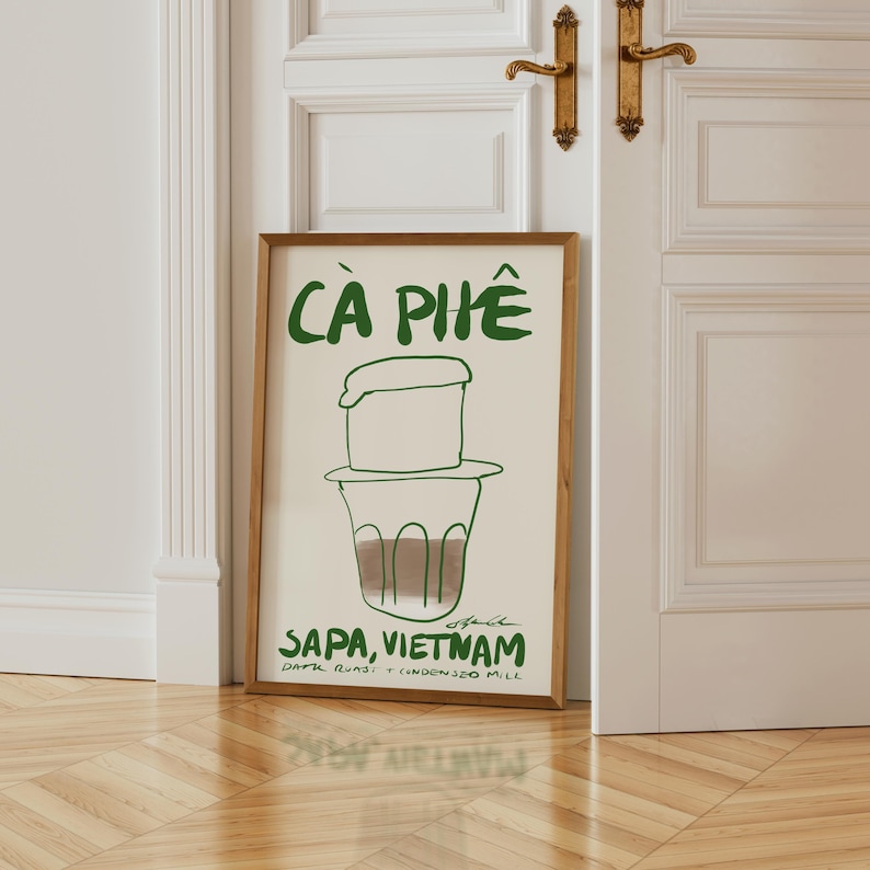 May include: A framed art print featuring a green illustration of Vietnamese coffee with the text "C&agrave; Ph&ecirc;" at the top. Below the coffee illustration is the text "Sapa, Vietnam". The print is in a wooden frame.