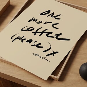 Puede incluir: Una impresi&oacute;n beige con texto negro a pinceladas que dice "one more coffee (please) x". La impresi&oacute;n est&aacute; en una bandeja de madera sobre una superficie de madera. La firma "Stephanie London" est&aacute; en la parte inferior.