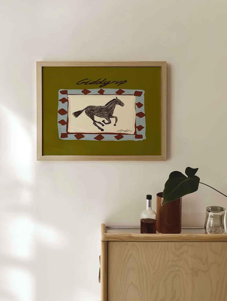 Puede incluir: Una impresi&oacute;n art&iacute;stica enmarcada con una ilustraci&oacute;n de un caballo corriendo. La obra de arte tiene un fondo verde con un dise&ntilde;o rectangular en azul y rojo. Las palabras "Giddy-up" est&aacute;n escritas encima del caballo.
