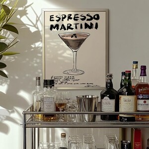 May include: A framed print displaying "Espresso Martini" and a cocktail illustration. A bar cart with bottles, glasses, and a metal ice bucket is in front of the print. The cart has two shelves and is made of metal.