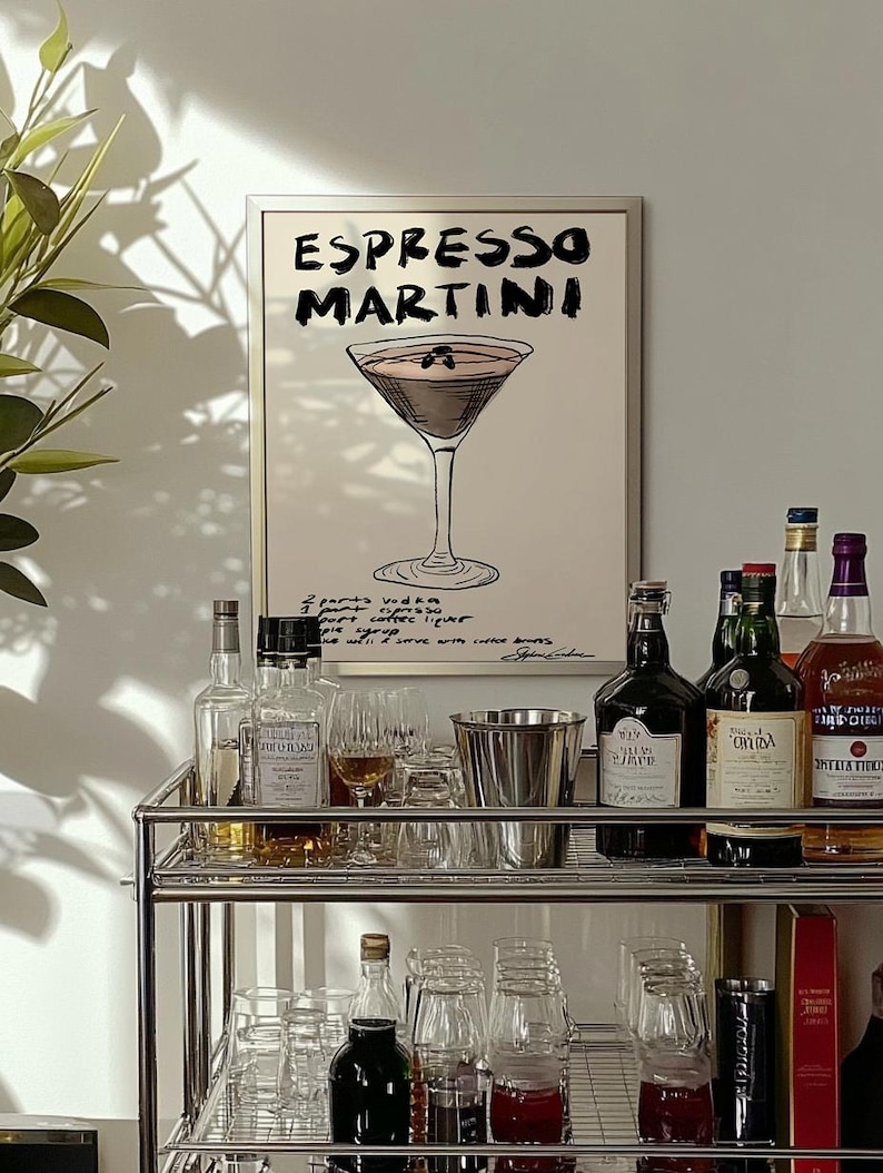 May include: A framed print displaying "Espresso Martini" and a cocktail illustration. A bar cart with bottles, glasses, and a metal ice bucket is in front of the print. The cart has two shelves and is made of metal.