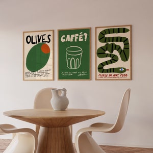 May include: Three framed art prints with text and illustrations hang above a wooden table and chairs. The prints feature the words "OLIVES", "CAFF&Eacute;?", and "PLEASE DO NOT FEED". The artwork includes a green olive, a coffee cup, and a green snake.