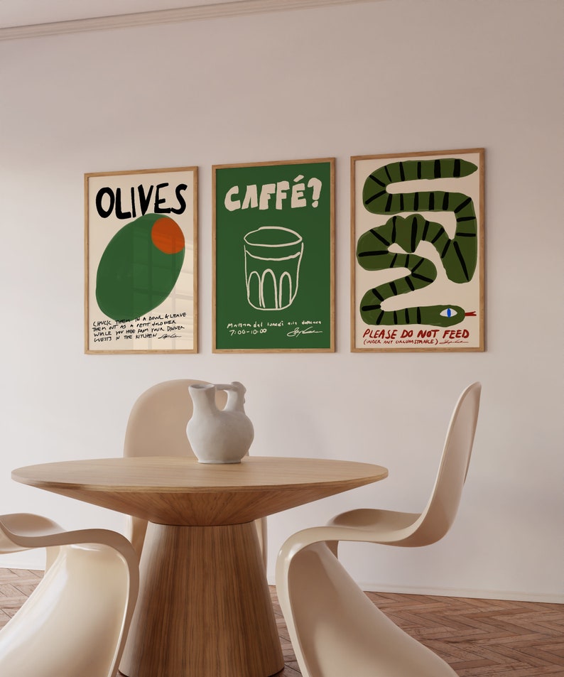 May include: Three framed art prints with text and illustrations hang above a wooden table and chairs. The prints feature the words "OLIVES", "CAFF&Eacute;?", and "PLEASE DO NOT FEED". The artwork includes a green olive, a coffee cup, and a green snake.
