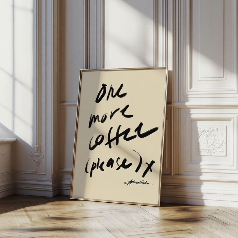 Puede incluir: Una impresi&oacute;n art&iacute;stica enmarcada con el texto "One more coffee (please) x" en trazos de pincel negros sobre un fondo crema. La impresi&oacute;n tiene un marco dorado y est&aacute; apoyada contra una pared blanca con molduras decorativas.