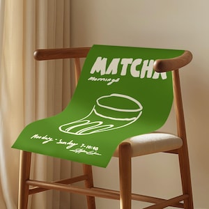 May include: A rectangular green poster featuring the white text MATCHA Mornings, a white line drawing of a cup, and the text Monday-Sunday 7-10:00. The poster is draped over a wooden chair with a light-colored seat, positioned near a curtain.