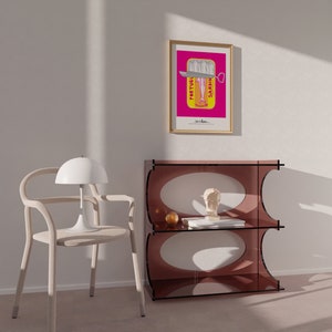 May include: A light-colored wooden chair with a white dome lamp, a translucent dark pink acrylic shelf unit with oval cutouts, and a framed poster featuring a sardine tin graphic with the text PORTUGUESE SARDINES in a bright pink background.