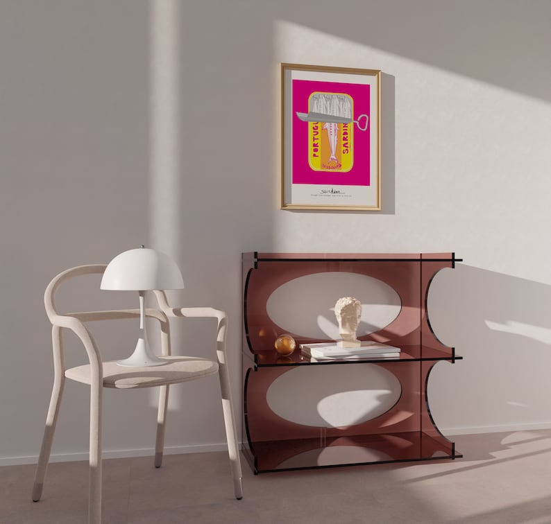 May include: A light-colored wooden chair with a white dome lamp, a translucent dark pink acrylic shelf unit with oval cutouts, and a framed poster featuring a sardine tin graphic with the text PORTUGUESE SARDINES in a bright pink background.