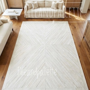 May include: A large, rectangular white rug with a geometric pattern of diagonal lines. The rug is centered on a hardwood floor, surrounded by light-colored furniture. The text "PIleandpalette" is visible on the rug.