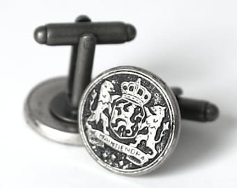 Puede incluir: Un par de gemelos de plata con un diseño en blanco y negro que presenta un escudo de armas con dos leones y una corona. El texto "Je Maintiendrai" es visible en los gemelos.