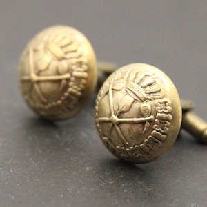 May include: A pair of gold cufflinks with a detailed design featuring a crown and other symbols.
