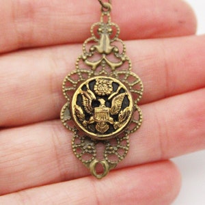 May include: A gold-toned pendant necklace with a black button featuring a gold eagle design. The pendant is ornate and has a filigree design.