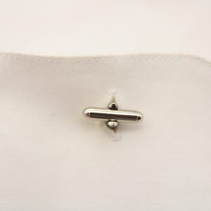 May include: Silver cufflinks with a cylindrical design and a small ball on each end.