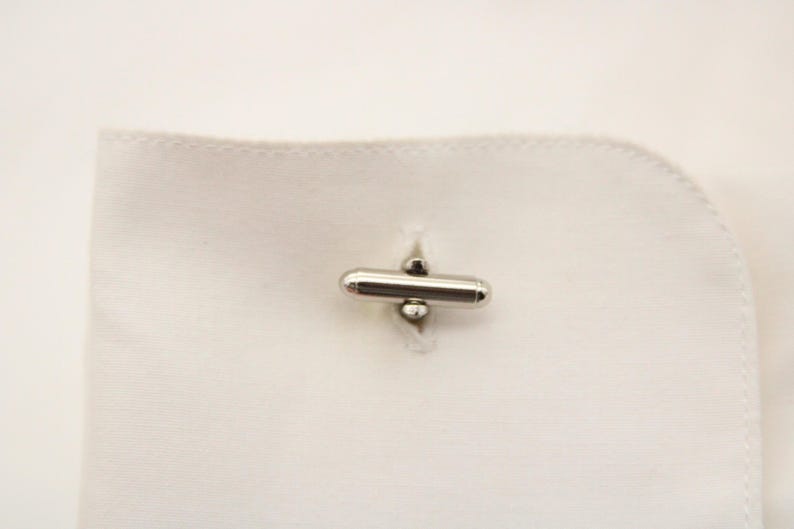 May include: Silver cufflinks with a cylindrical design and a small ball on each end.