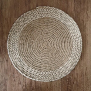 Op de afbeelding: Een ronde, geweven jute placemat met een spiraalvormig ontwerp. Het midden is een lichtere bruintint en de rand is een iets donkerder, getextureerde weefsel. De placemat ligt op een houten ondergrond.