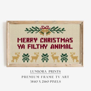 May include: Framed art print with a beige knit-style background. The text "MERRY CHRISTMAS YA FILTHY ANIMAL" is in burgundy and red. The top has green and gold accents, and the bottom has reindeer and evergreen designs. The frame is light brown.