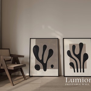 May include: Two framed rectangular wall art prints featuring black organic, abstract shapes set against a light beige background. Each print is enclosed in a thin black frame, displaying distinct, fluid, plant-like silhouettes.
