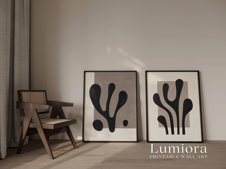 May include: Two framed rectangular wall art prints featuring black organic, abstract shapes set against a light beige background. Each print is enclosed in a thin black frame, displaying distinct, fluid, plant-like silhouettes.