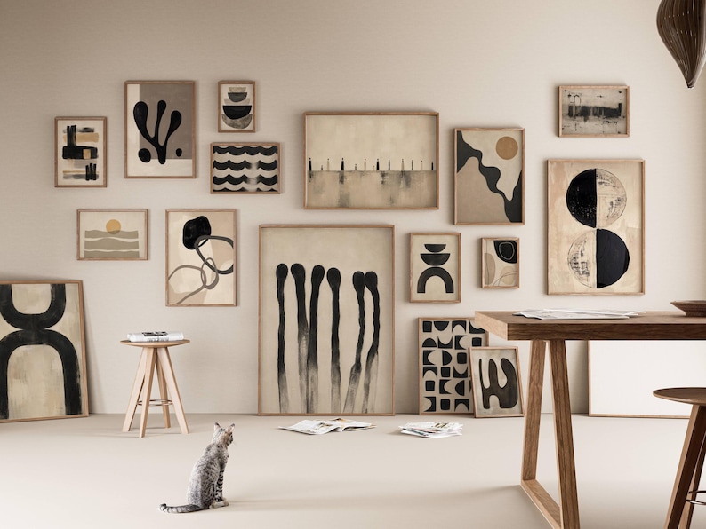 May include: A gallery wall featuring a collection of framed abstract art prints in neutral tones of beige, black, and white. The artwork displays various geometric shapes, organic forms, and linear patterns, all housed in light-colored wooden frames.