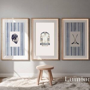 May include: Three framed wall art prints featuring hockey-themed illustrations. The prints include a hockey helmet, a jersey, and crossed hockey sticks. Each print has a blue and white striped background and a wooden frame.
