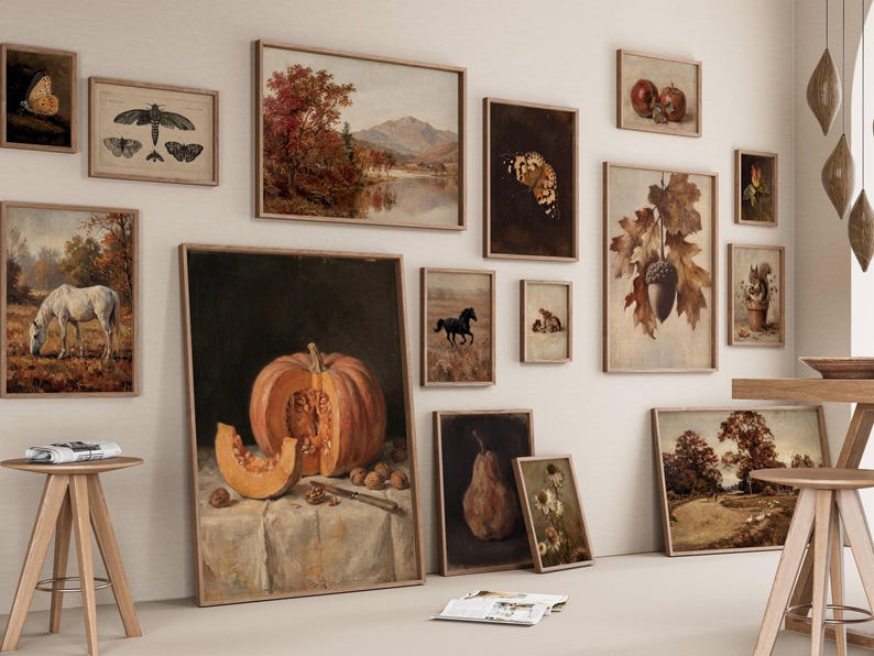Puede incluir: Una composici&oacute;n de pared de galer&iacute;a con m&uacute;ltiples l&aacute;minas de arte enmarcadas con temas oto&ntilde;ales, incluyendo un bodeg&oacute;n de calabaza, un caballo blanco en un campo, insectos, una pera, bellotas y paisajes, expuestos en una pared clara.
