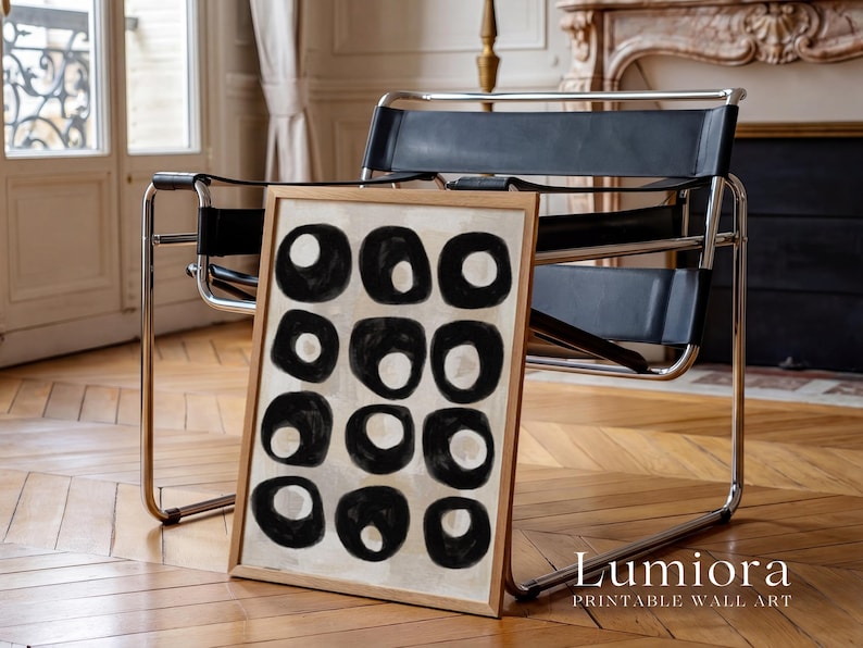 May include: A framed rectangular wall art print featuring a grid of twelve black hand-painted circular shapes on a light beige background. The artwork is encased in a light-colored wooden frame. The text "Lumiora PRINTABLE WALL ART" is visible.