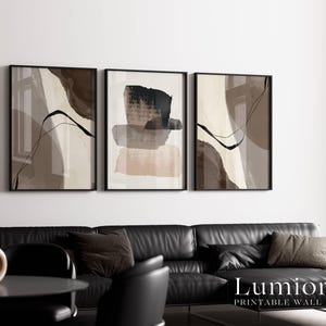 May include: A set of three framed wall art prints featuring abstract compositions in shades of brown, beige, and black. The artwork displays layered brushstrokes, fluid lines, and organic shapes. The text "Lumiora PRINTABLE WALL ART" is visible.