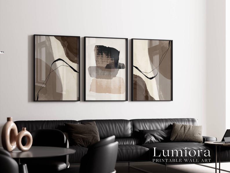 May include: A set of three framed wall art prints featuring abstract compositions in shades of brown, beige, and black. The artwork displays layered brushstrokes, fluid lines, and organic shapes. The text "Lumiora PRINTABLE WALL ART" is visible.