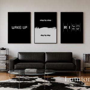 May include: Three rectangular wall art prints in black frames. The left print has a black background with the white text WAKE:UP. The center print is split horizontally with step by step on black and day by day on white. The right print says RICH RISK.
