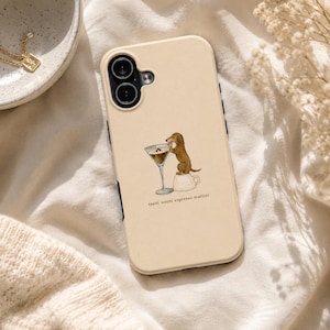 Op de afbeelding: Een beige smartphonehoesje met een bruine teckel die op een wit koffiekopje naast een martiniglas staat. De tekst "teeni weeni espresso martini" is in kleine zwarte letters onder de illustratie van de hond en de glazen gedrukt.