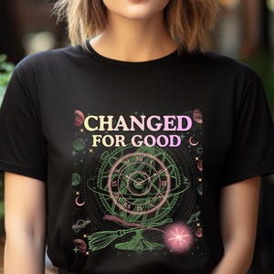 May include: Black t-shirt with the text "CHANGED FOR GOOD" in a gradient of pink and yellow. The shirt features a detailed graphic of a clock, planets, and a broom, with pink and green accents.