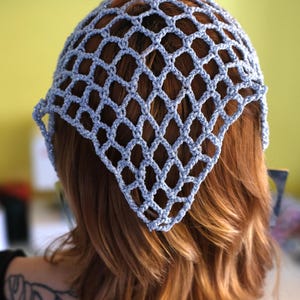 Pode incluir: Uma touca de croch&ecirc; azul claro com um padr&atilde;o em forma de diamante. A touca &eacute; usada sobre cabelos castanhos avermelhados. A touca tem formato triangular e cobre a parte superior da cabe&ccedil;a.
