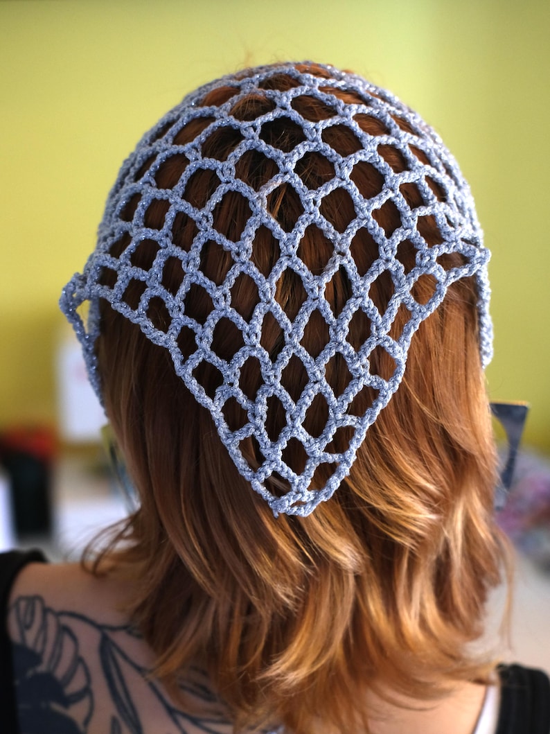 Pode incluir: Uma touca de croch&ecirc; azul claro com um padr&atilde;o em forma de diamante. A touca &eacute; usada sobre cabelos castanhos avermelhados. A touca tem formato triangular e cobre a parte superior da cabe&ccedil;a.