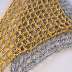 Pode incluir: Close-up de dois tecidos de rede de croch&ecirc;. Um &eacute; dourado, o outro prateado. A trama aberta da rede cria uma textura delicada e arejada. Os tecidos s&atilde;o provavelmente usados para fins decorativos ou como acess&oacute;rios de moda.