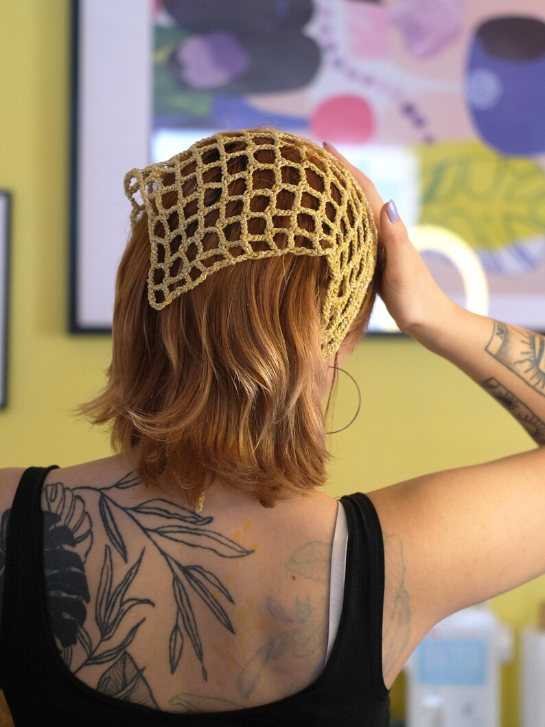 Pode incluir: Uma touca de croch&ecirc; bege com um design em forma de rede. A touca &eacute; usada na cabe&ccedil;a. A pessoa na imagem est&aacute; usando uma regata preta e tem uma tatuagem no bra&ccedil;o e nas costas.